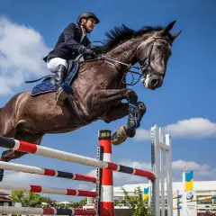 Un cavalier et son cheval réalisent un saut d'équitation spectaculaire dans un ciel bleu.
