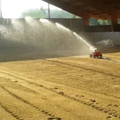 Arrosage d'une carrière équestre par un système mobile, créant un voile d'eau sur le sable.