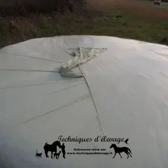 Gros plan sur une botte de matière sèche enrubannage, protégée par une bâche blanche tendue.
