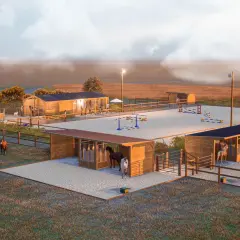 Vue d'une écurie de propriétaire avec plusieurs chevaux, des boxes, une carrière d'obstacles et un manège.