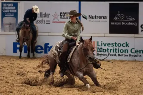 Une cavalière effectue un virage serré, soulevant de la poussière avec son cheval lors d'une compétition de cutting cheval.