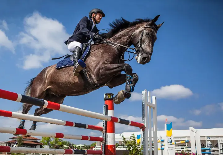 Un cavalier et son cheval réalisent un saut d'équitation spectaculaire dans un ciel bleu.