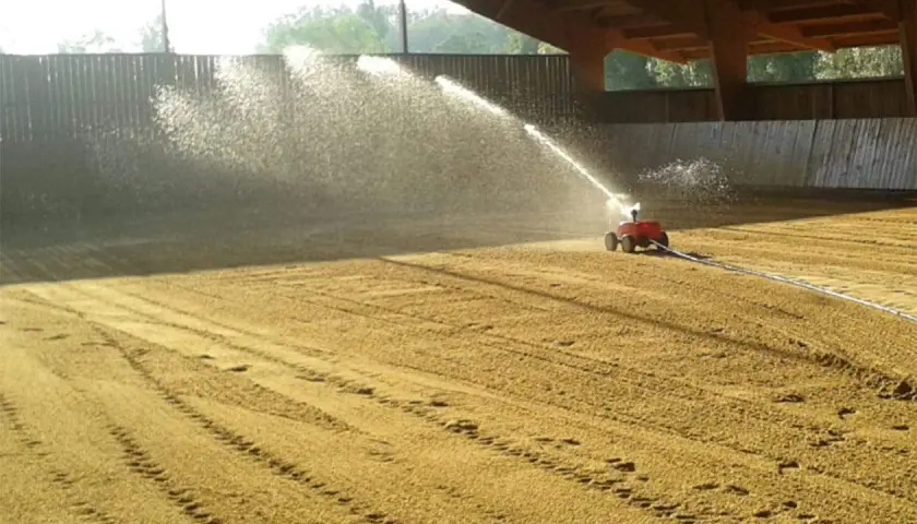Arrosage d'une carrière équestre par un système mobile, créant un voile d'eau sur le sable.