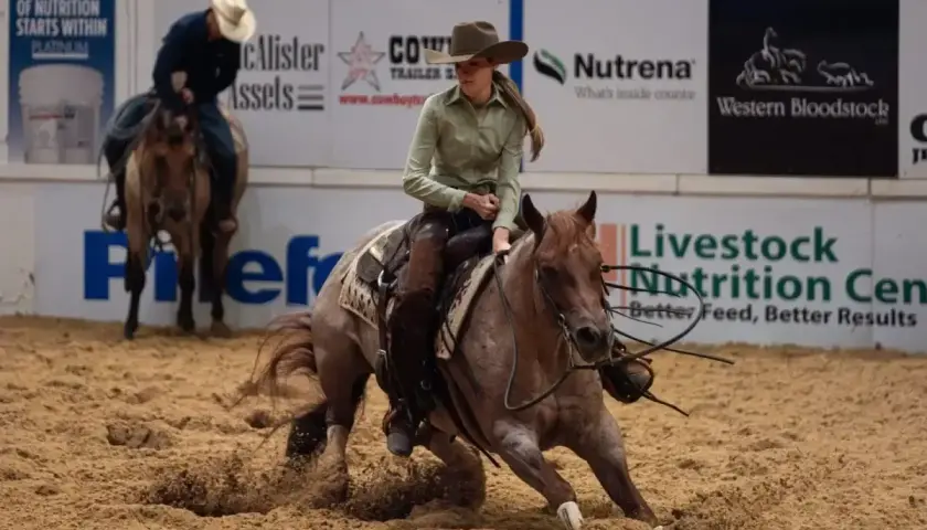 Une cavalière effectue un virage serré, soulevant de la poussière avec son cheval lors d'une compétition de cutting cheval.