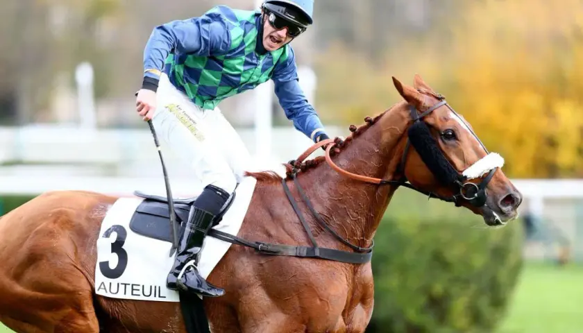 Un jockey en tenue bleue et verte, sur un cheval bai portant le numéro 3 "Auteuil", sprinte vers la victoire.