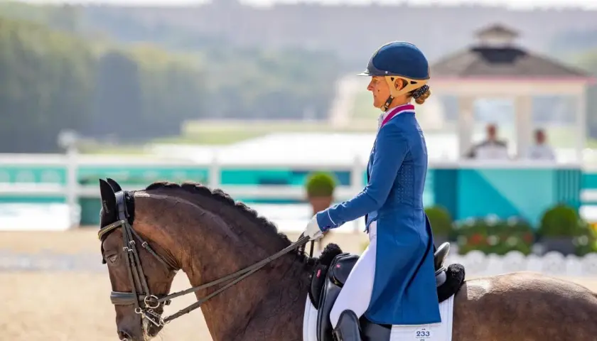 Cavalier pro en tenue d'apparat, concentrée sur sa reprise de dressage. Le cheval, fier, est prêt pour la compétition.