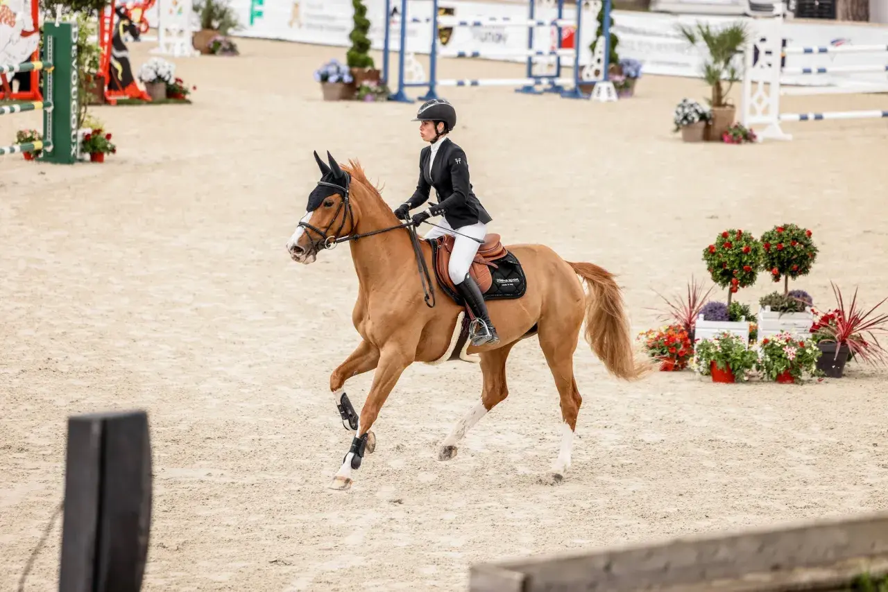 Une cavalière en tenue d'équitation exécute un volte cheval sur une piste de sable, entourée de décorations florales.