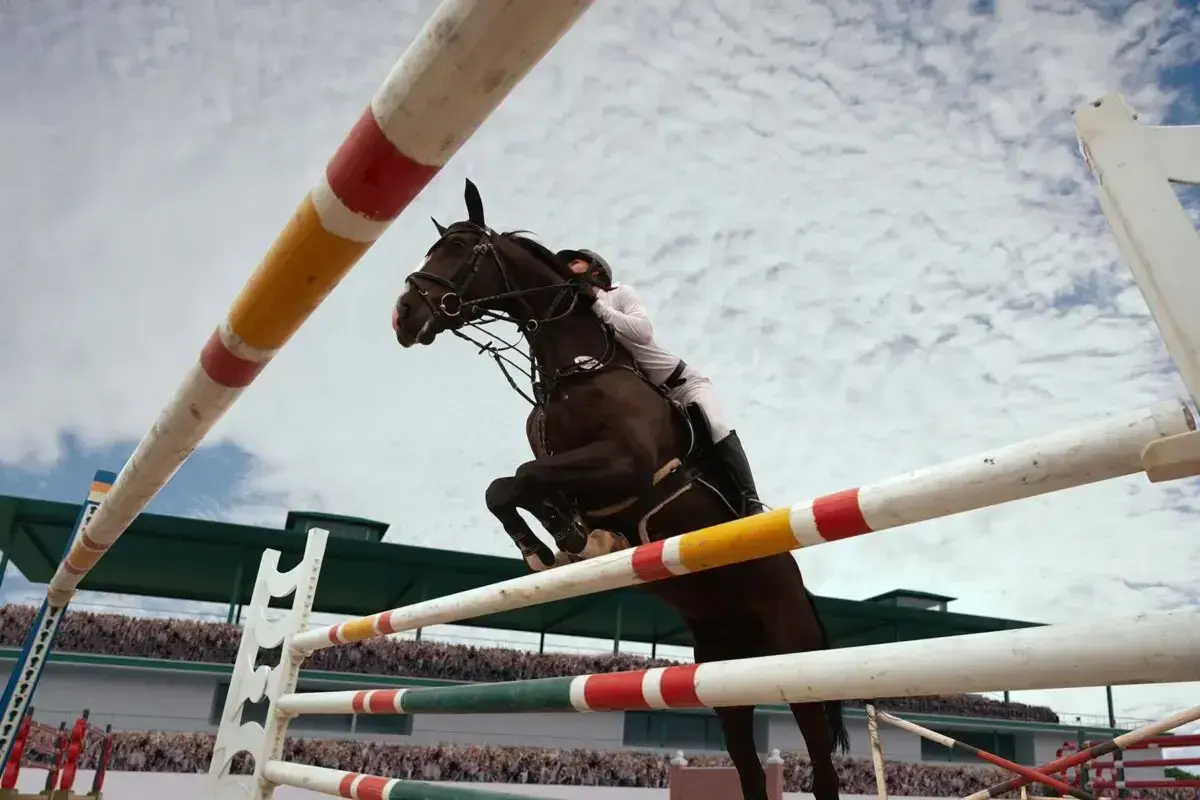 Un cheval brun saute par-dessus une barrière dans une carrière de saut d'obstacle, sous un ciel nuageux.