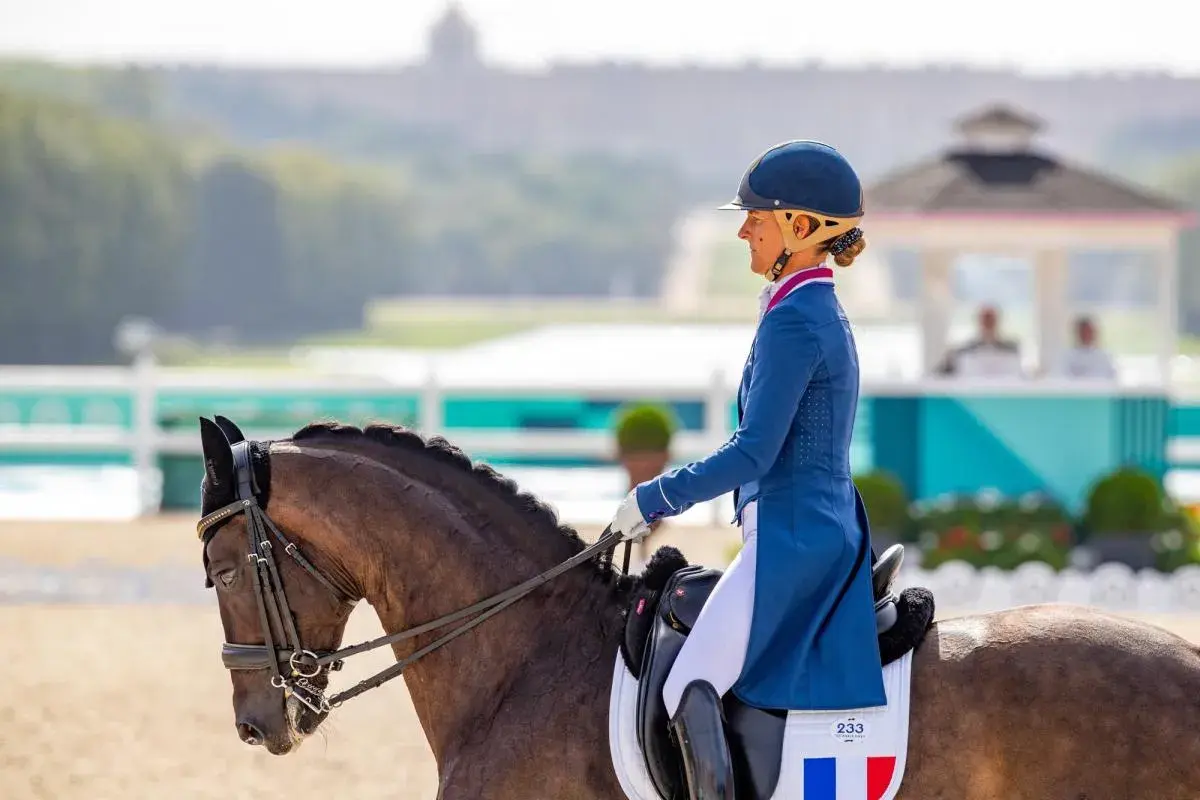 Cavalier pro en tenue d'apparat, concentrée sur sa reprise de dressage. Le cheval, fier, est prêt pour la compétition.
