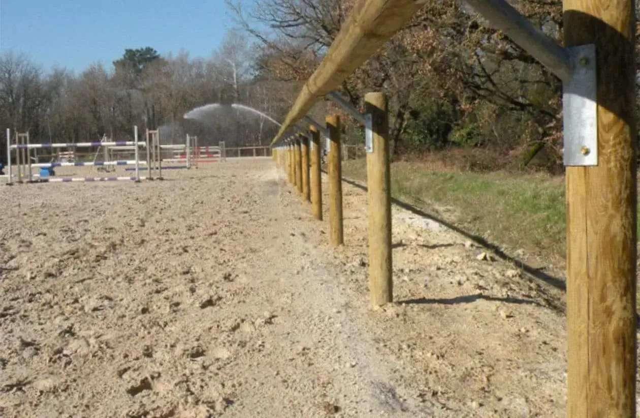 Piste d'équitation arrosée, avec obstacles et clôture en bois. La réglementation carrière équestre assure la sécurité et la qualité des installations.