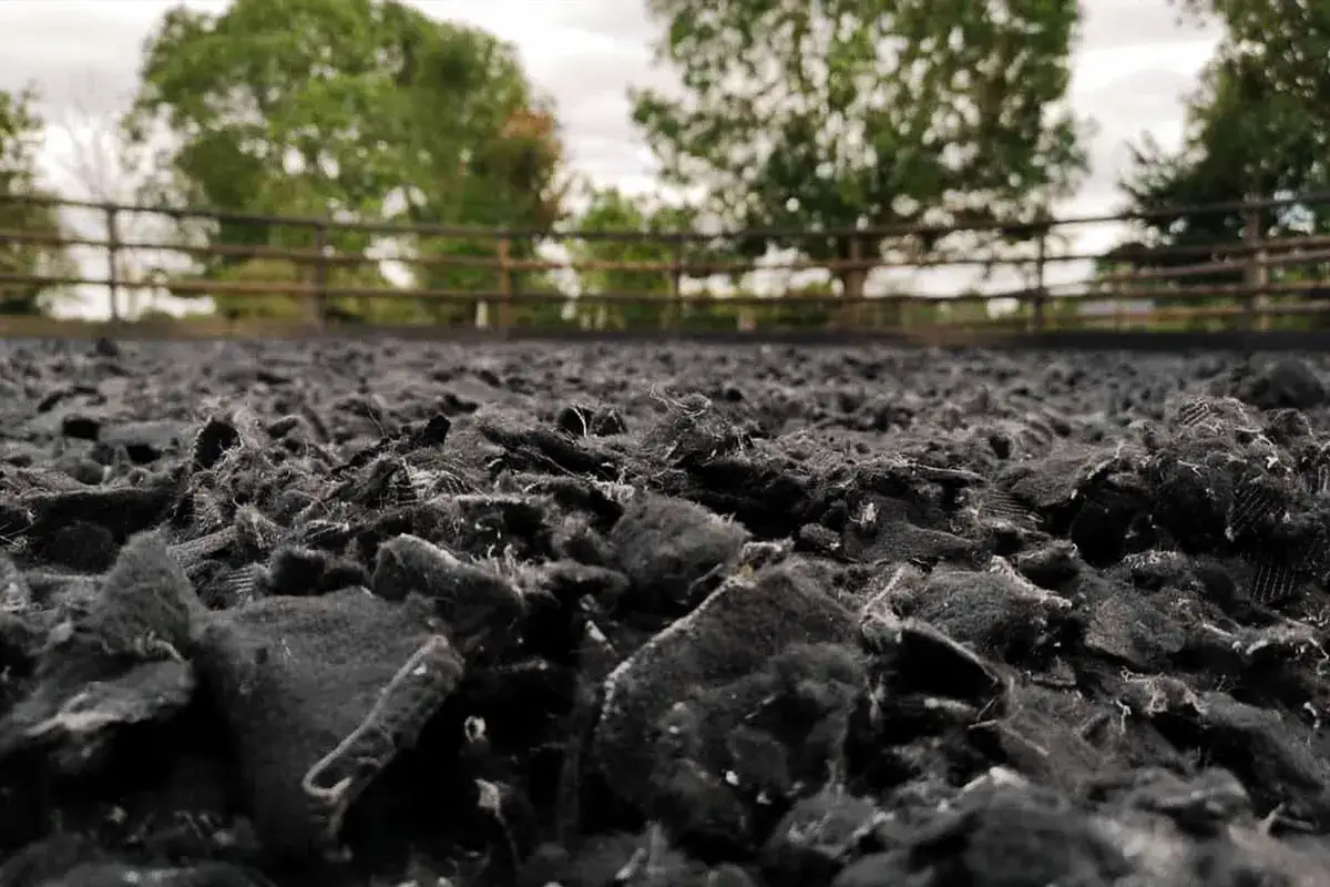 Gros plan sur le sol d'une carrière équestre, composé de copeaux noirs. Le système d'arrosage est prêt pour maintenir la piste en parfait état.
