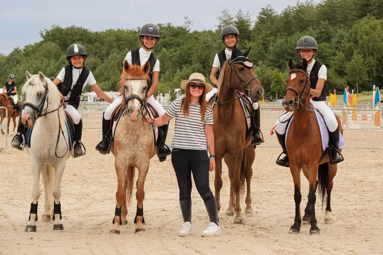 Des jeunes cavaliers et leur monitrice posent fièrement après avoir fait de l'équitation.